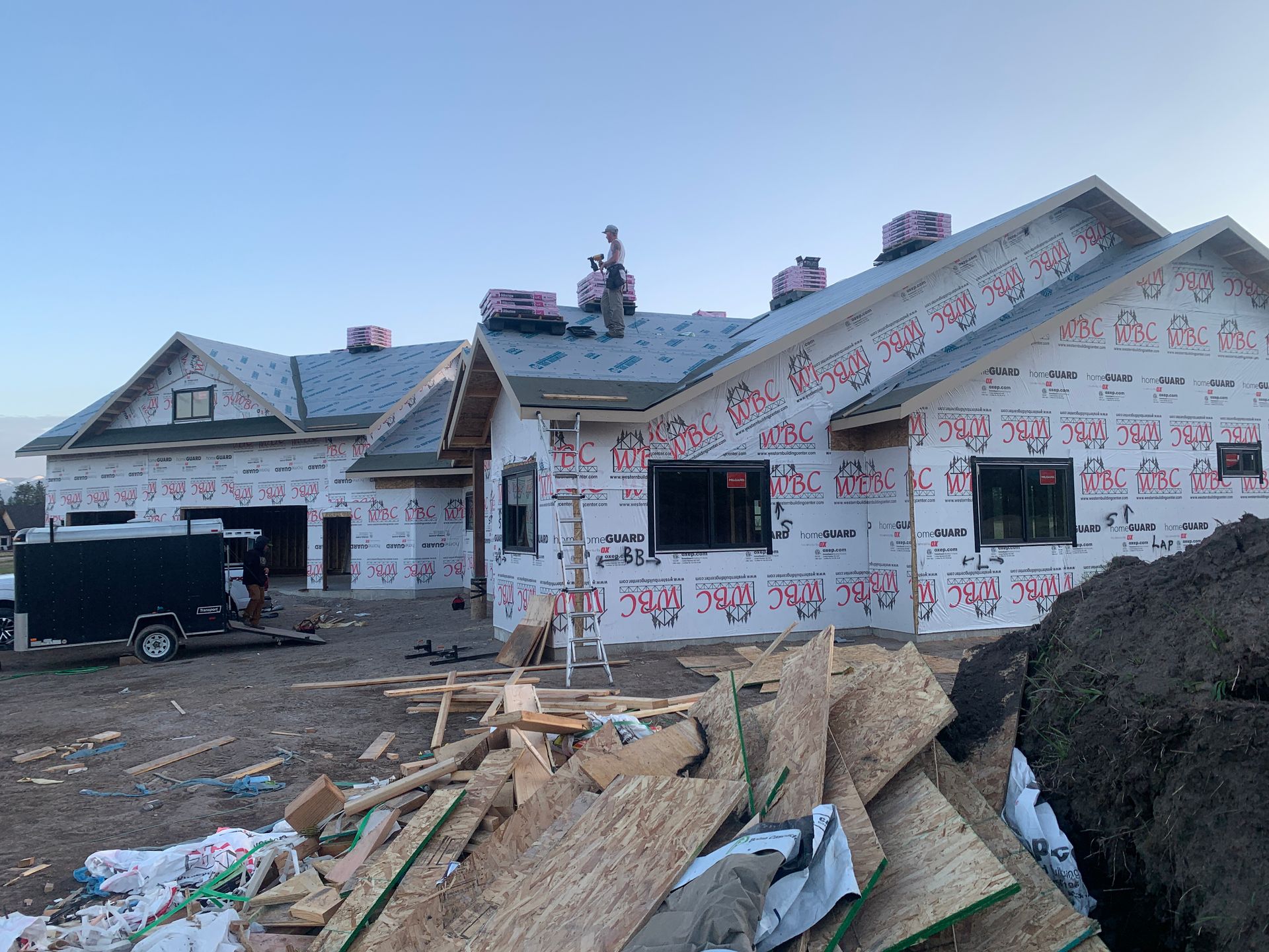 Partially built house wrapped in Tyvek, with construction materials piled in front at dusk