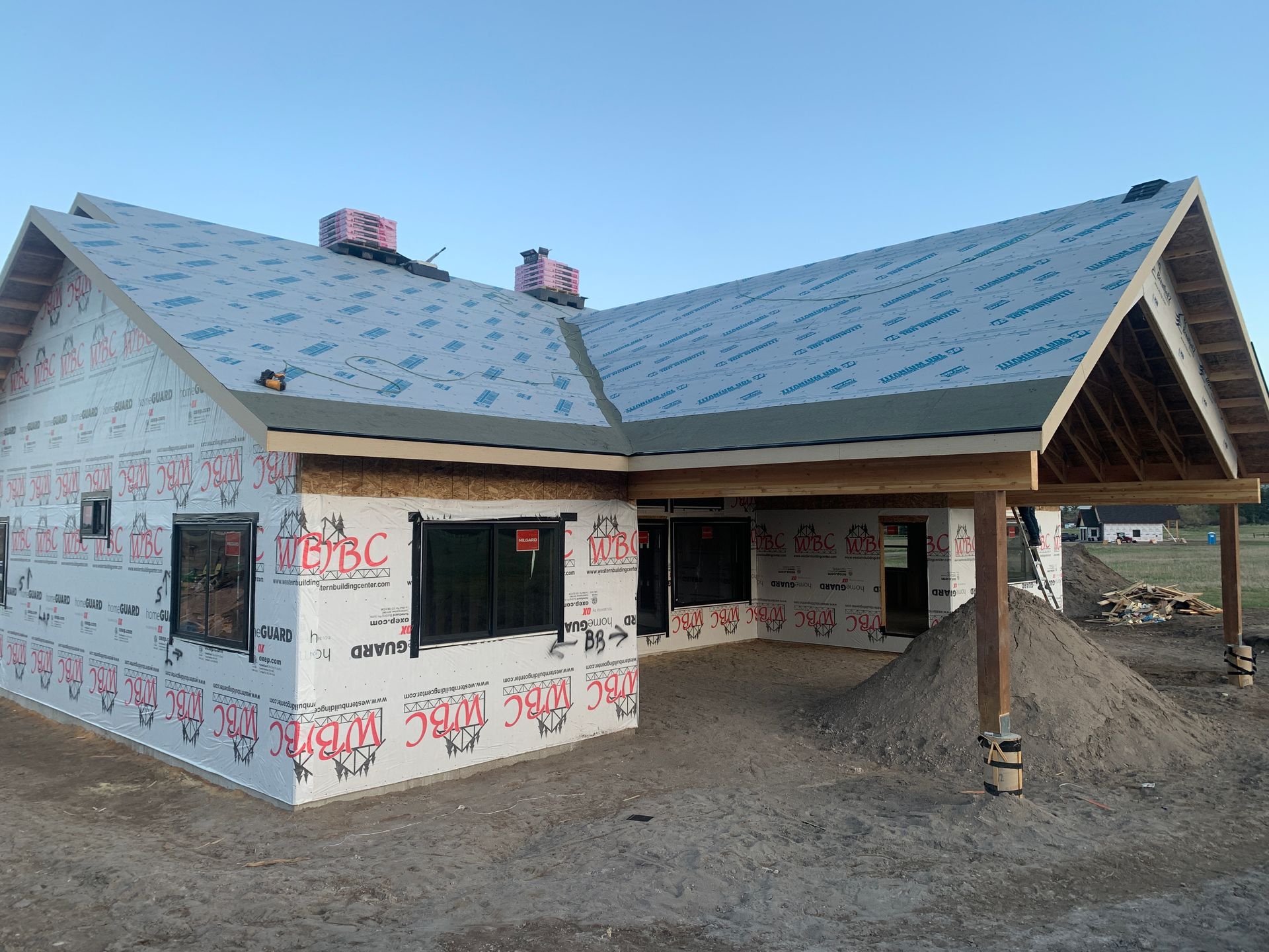 Partially built house with blue roof, exposed walls, and porch on a dirt lot