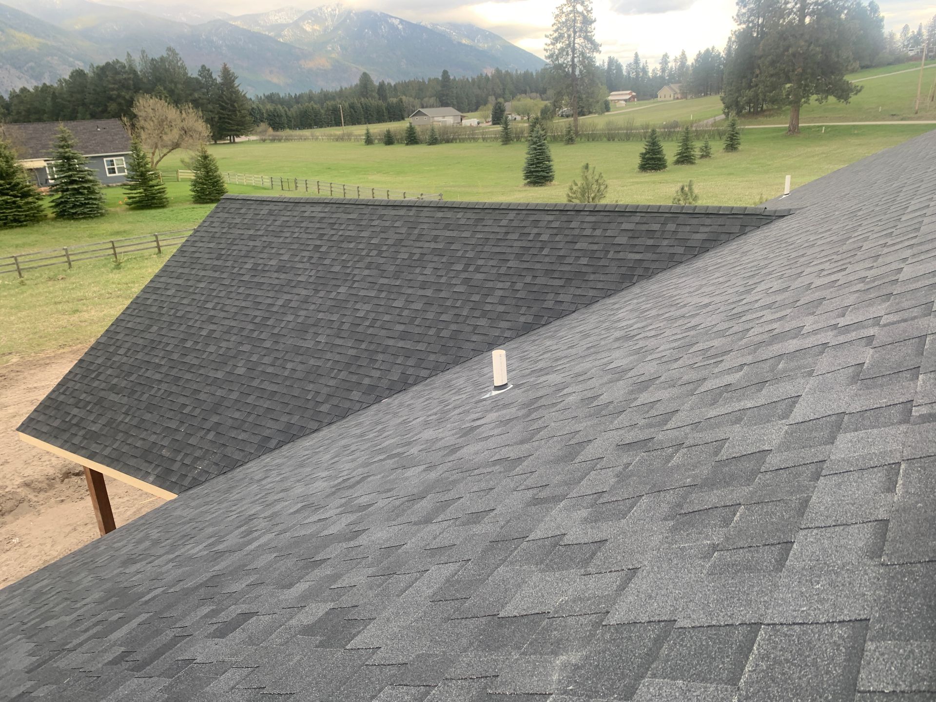 Dark gray shingled rooftops in front of a green meadow and distant mountains.