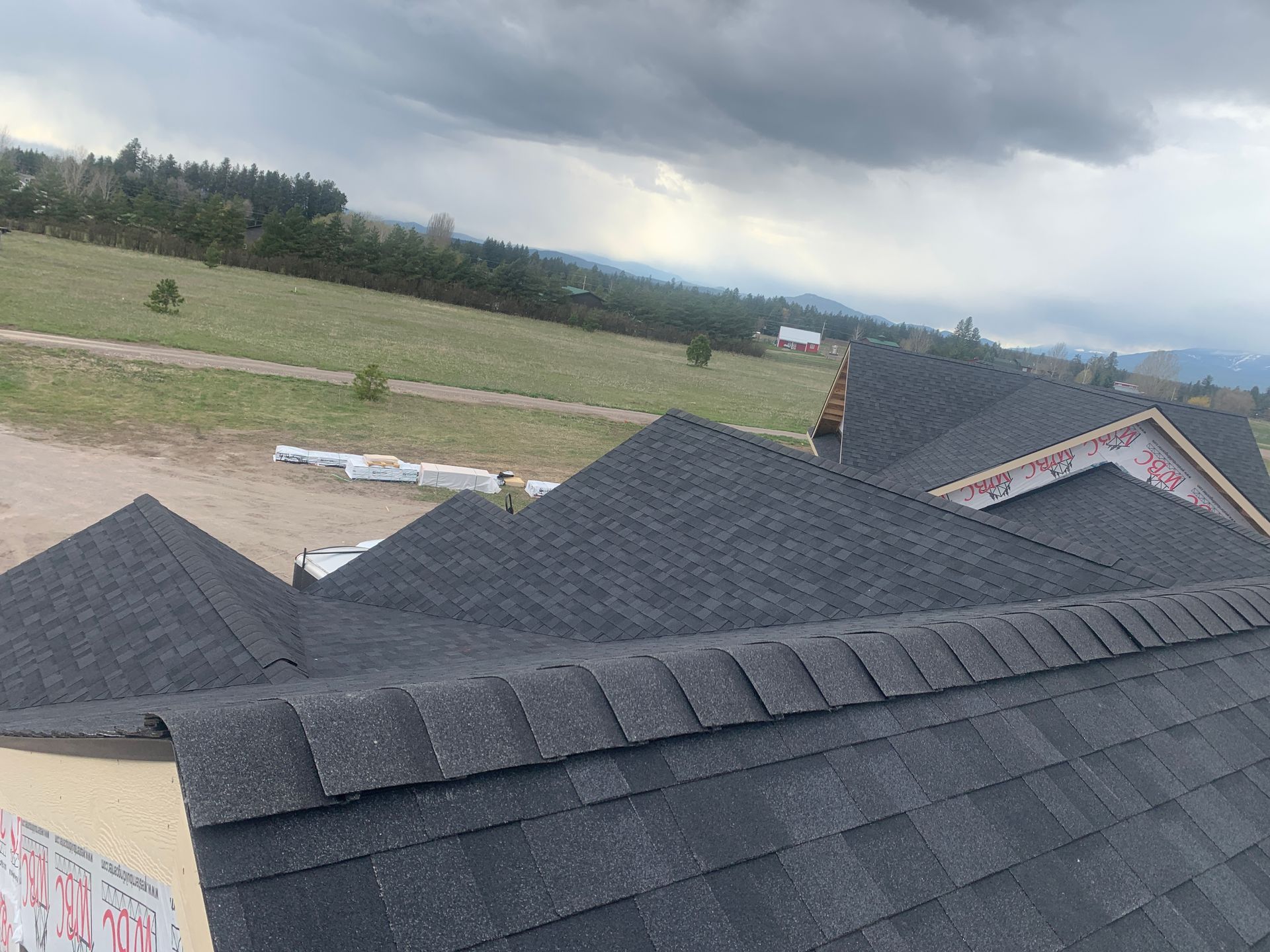 Dark shingled rooftops under a cloudy sky with fields in the background