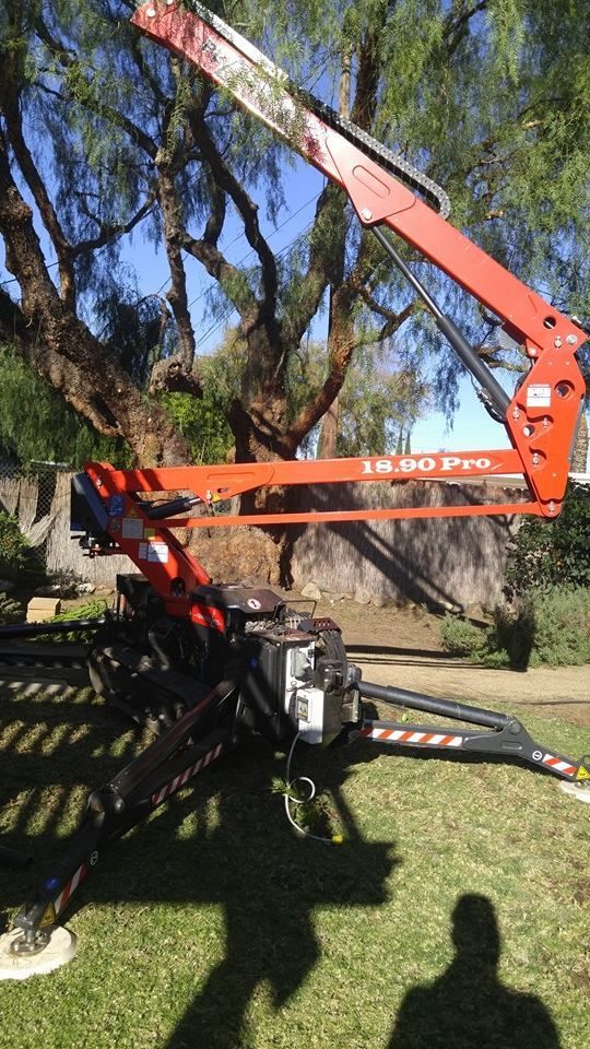 Orange boom lift raised among trees on a grassy lawn, with people’s shadows in the foreground