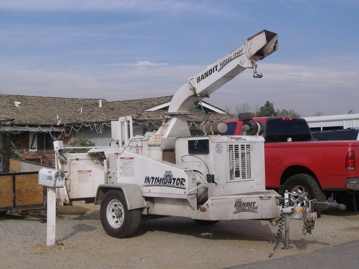 White utility bucket truck parked beside a red pickup in a dusty lot under a blue sky