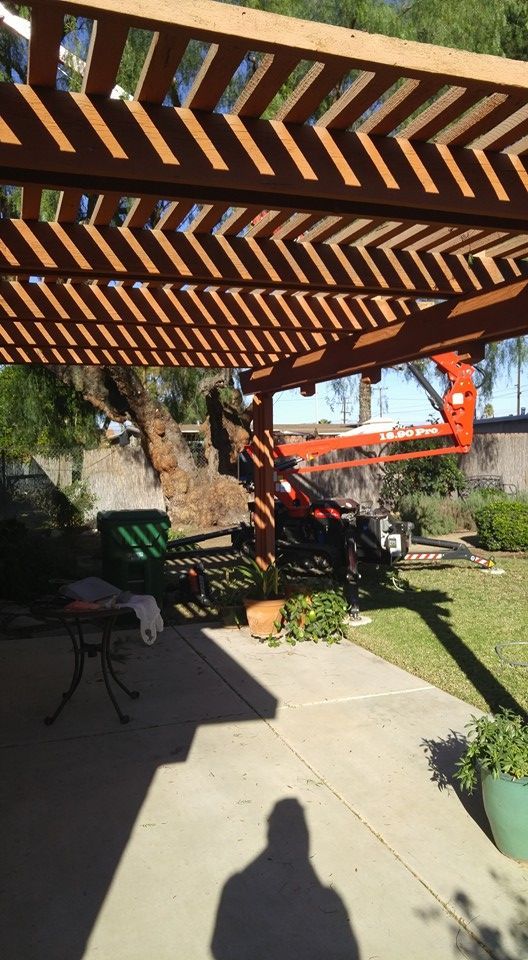 Backyard patio under a wooden pergola with a concrete path, lawn, potted plants, and a folded chair.