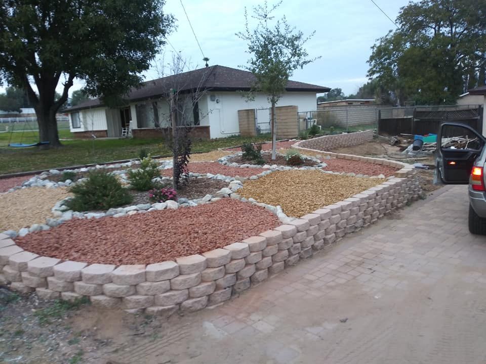 Front yard with raised stone flower beds, mulch, shrubs, and a house beside a driveway