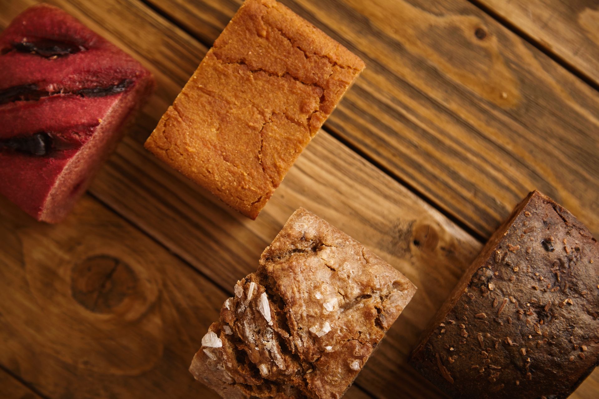 Cuatro rebanadas de diferentes tipos de pan sobre una mesa de madera: rojo, tostado, marrón y marrón oscuro.
