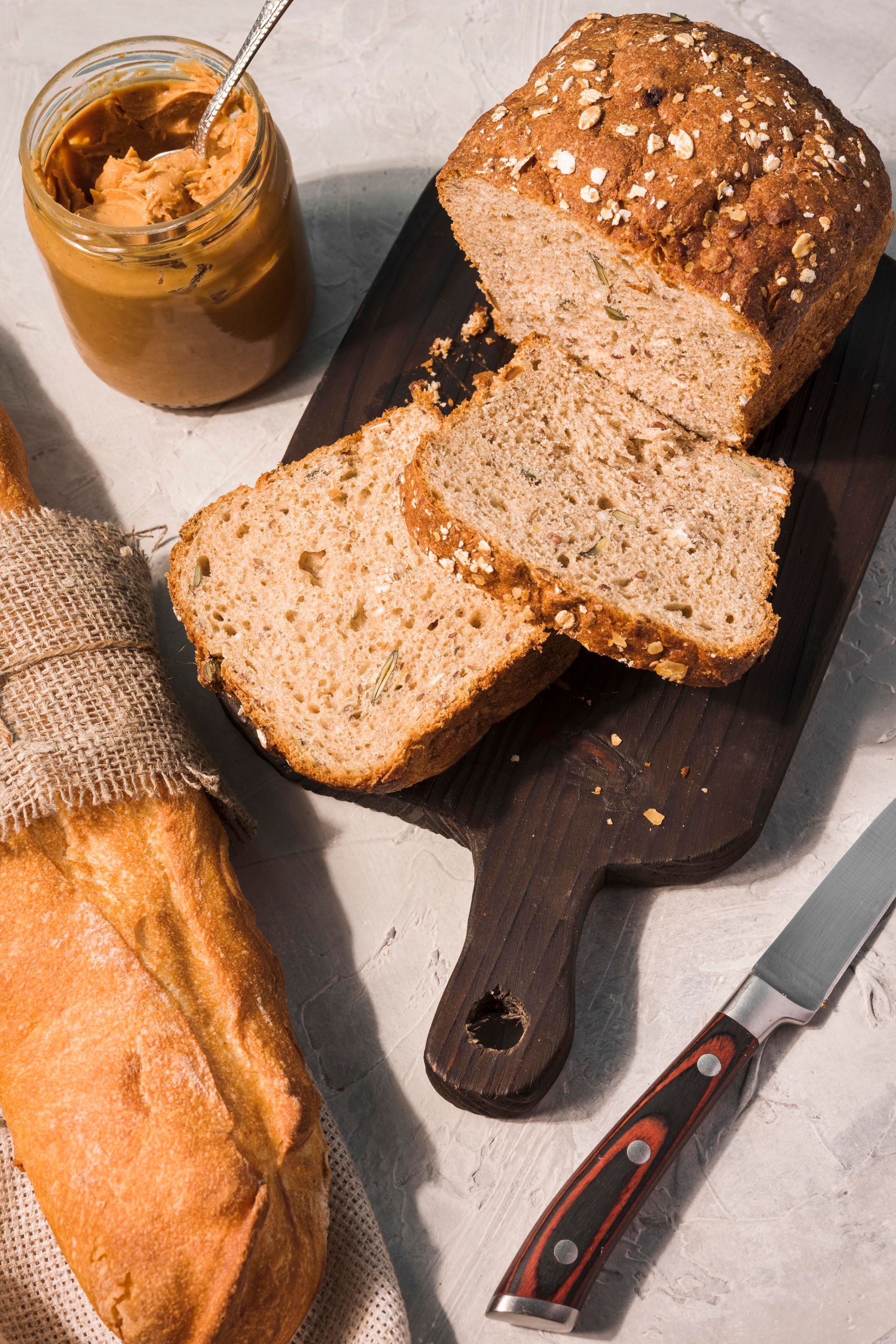 Pan con trozos cortados sobre una tabla de cortar, frasco de pasta para untar, baguette y cuchillo.