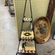 Thrift store display with a patterned ladder shelf and a decorative oval tray leaning beside it.