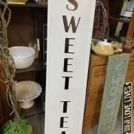 Vertical sign reading “SWEET TEA” in a rustic indoor display with bowls and home decor