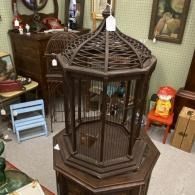 Decorative dark wood birdcage on a table in a living room, with a small bird inside.