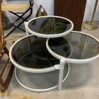 Three round glass-top nesting coffee tables with white frames and dark mirrored shelves indoors