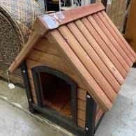 Small wooden doghouse with red shingled roof and arched entrance on a concrete floor