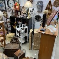 Assorted vintage furniture and decor displayed in a shop, including lamps, shelves, baskets, and tables.