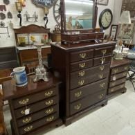 Antique dark wood dressers with brass pulls in a vintage shop, topped with mirrors and decor