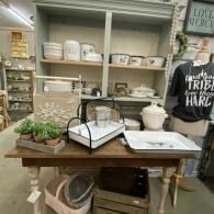 Rustic store display table with white ceramics, serving trays, plants, and a black wire basket