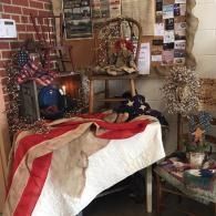 Festive holiday display with a bed draped in red and white cloth beside a brick fireplace and decorated tree