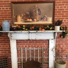 Decorated white fireplace mantel with pumpkins, fall flowers, and framed art against a brick wall