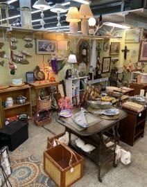 Cluttered antique shop with vintage furniture, lamps, wall decor, and a dining table display