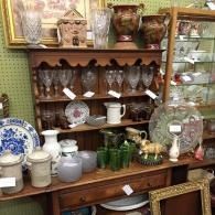 Antique shop shelf with glassware, pottery, and decorative plates in a crowded display