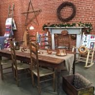 Rustic patio with wooden dining table, chairs, brick wall, fireplace mantel, and decorative star and wreath.