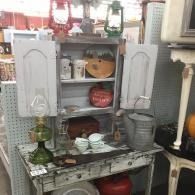 Cluttered kitchen shelf with dishes, jars, pots, and a green bottle under gray cabinets