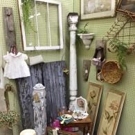 Outdoor garden display with hanging white shirt, framed art, mirror, lantern, and woven baskets on a fence