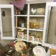 White hutch filled with vintage dishes and glassware, with decorative plates and baskets displayed below.