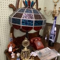 Colorful stained-glass lamp on a wooden table with vintage bottles, phones, and decor items