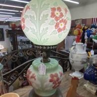 Vintage floral table lamp with frosted globe shade and pastel pink-and-green ceramic base in an antique shop