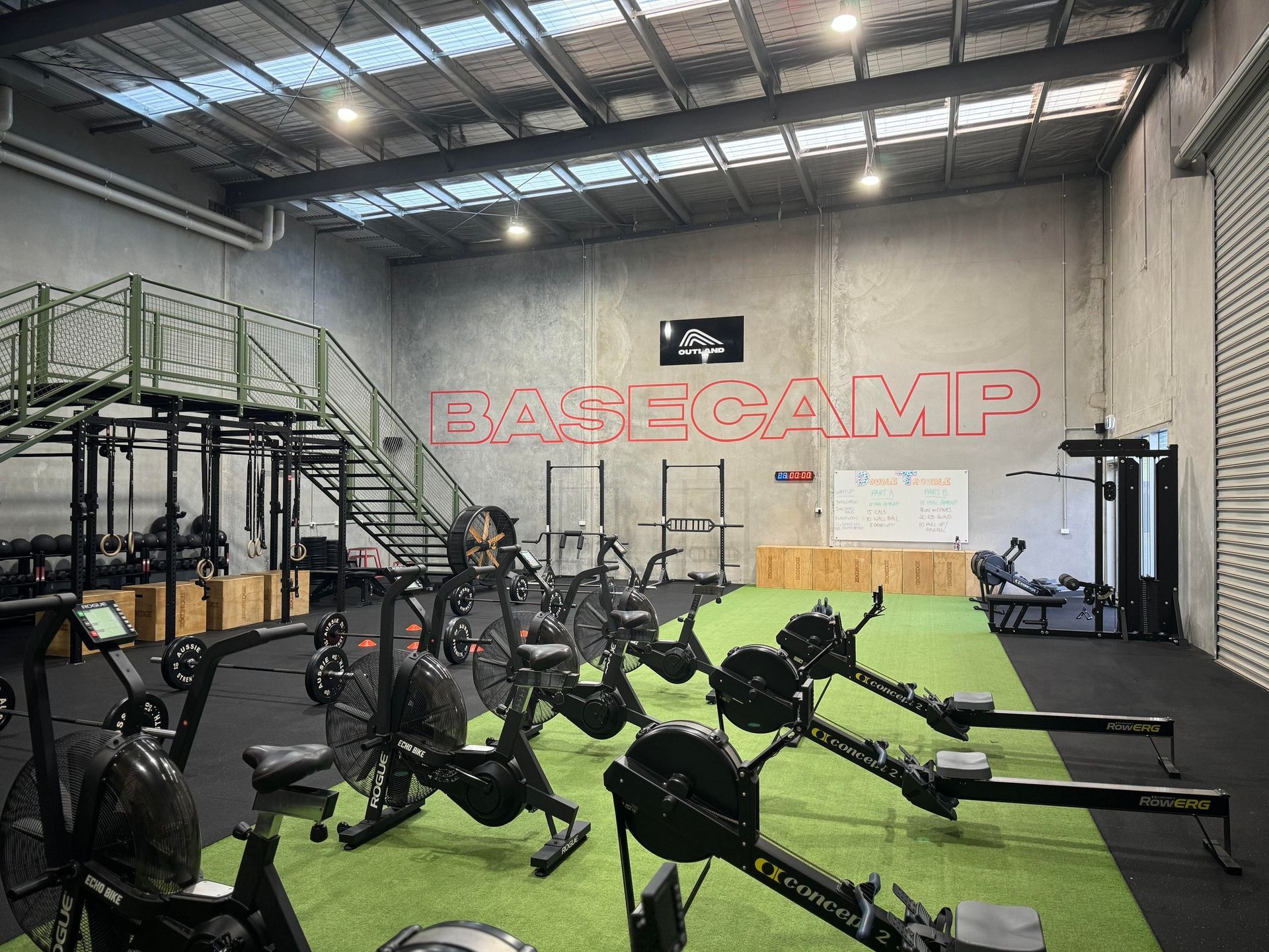 Indoor gym with rowing machines on turf and a large red “BLAZEGAMP” sign on the wall