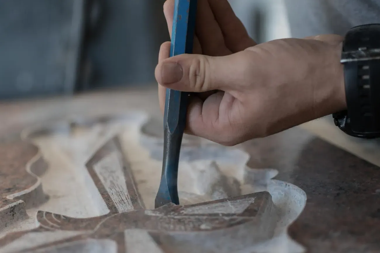Hand using a blue tool to carve a wooden object on a workbench