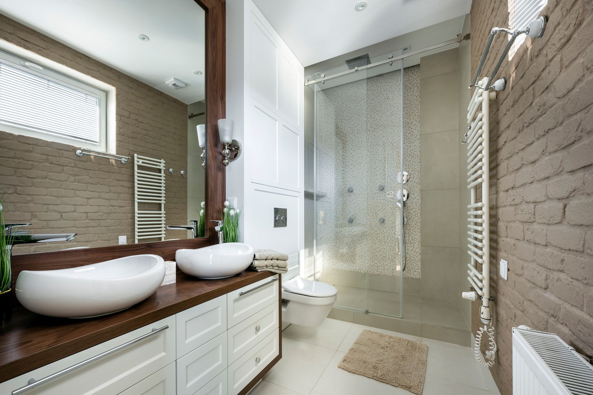 Modern bathroom with double vessel sinks, large mirror, and glass shower in a neutral, tiled interior