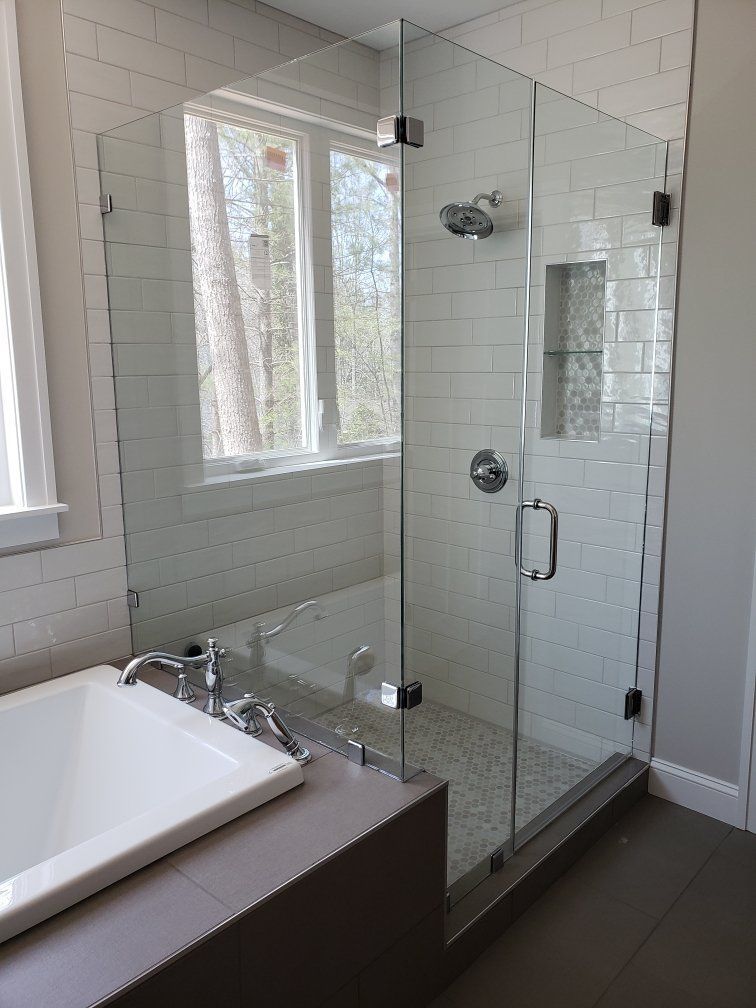 Modern bathroom with glass-enclosed shower, white tile walls, and a tub by the window Modern bathroom with glass-enclosed shower, white tile walls, and a tub by the window