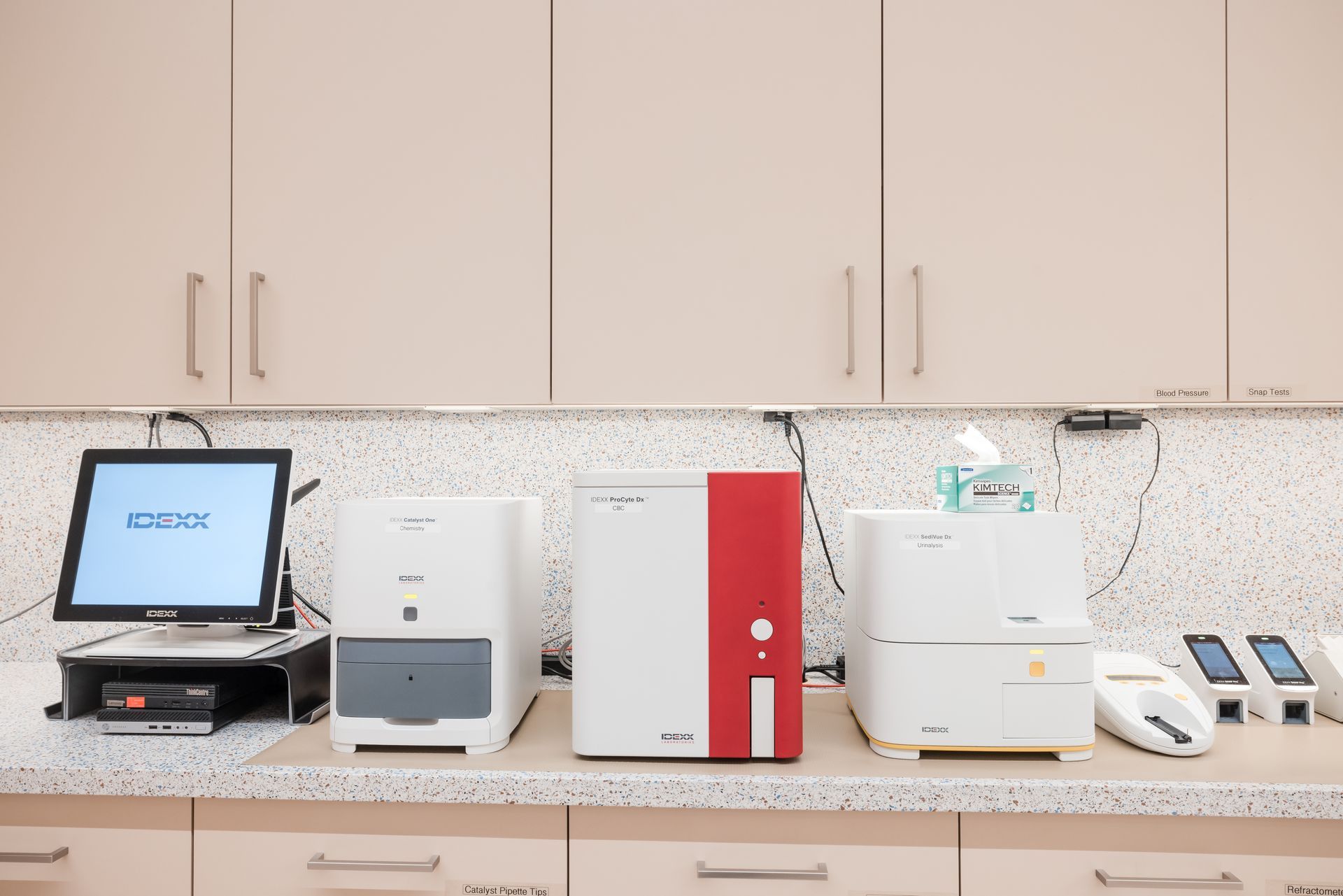 Desktop printers and office equipment lined up on a countertop under beige cabinets