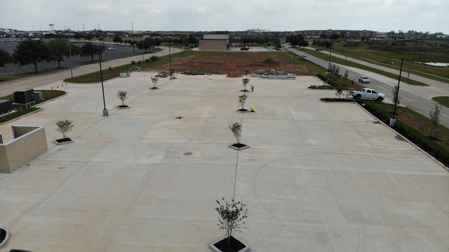 An aerial view of a parking lot with trees and a road in the background.