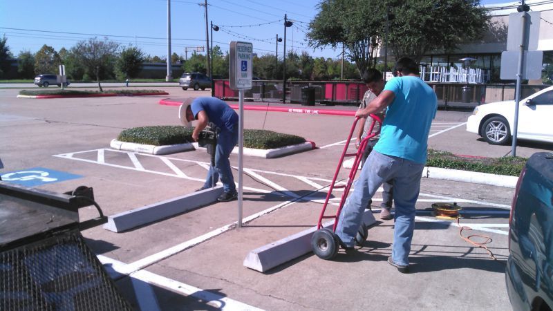 Two men are working in a parking lot and one is pushing a dolly