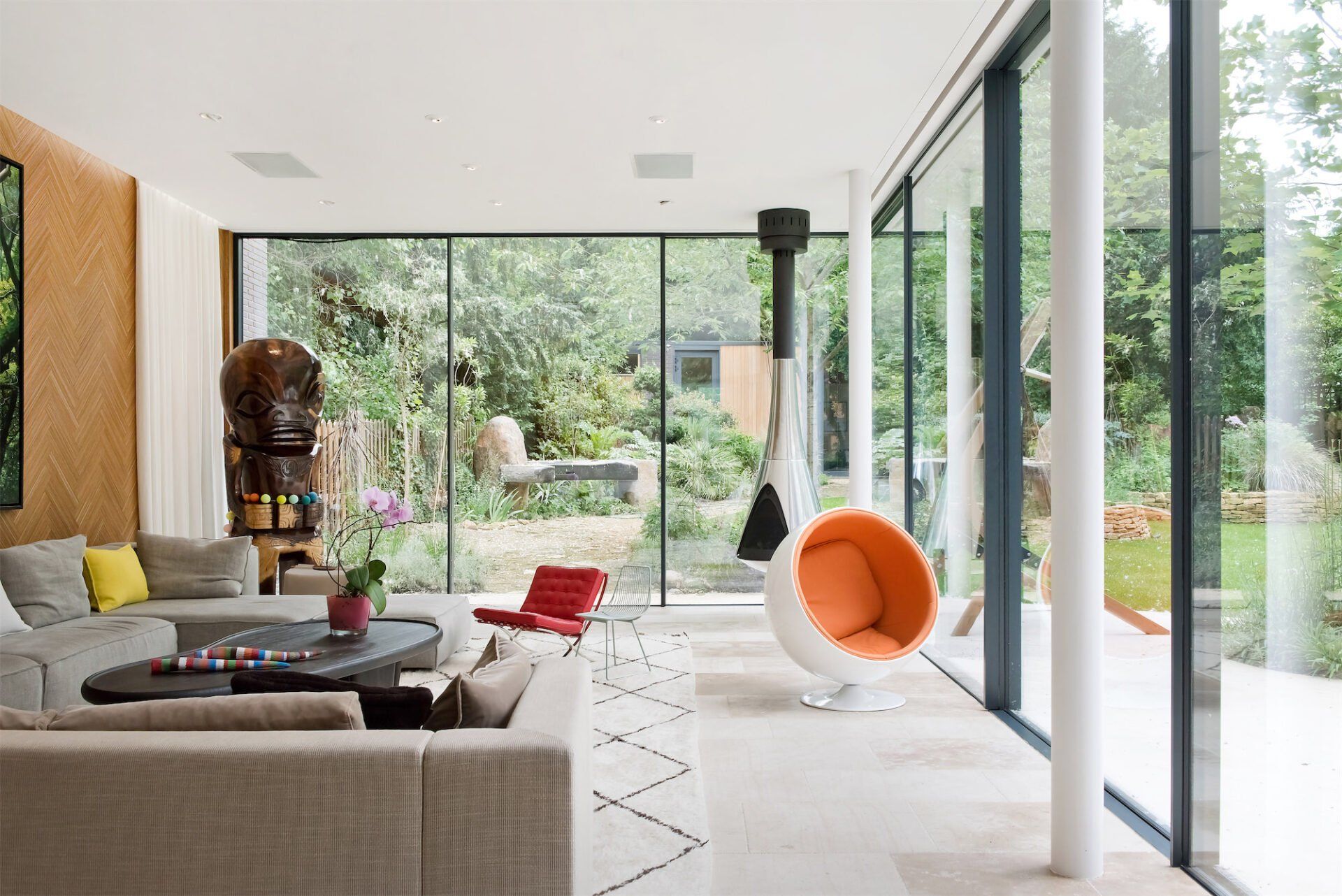 Modern living room with beige sofa, red chair, large glass doors, and lush garden view