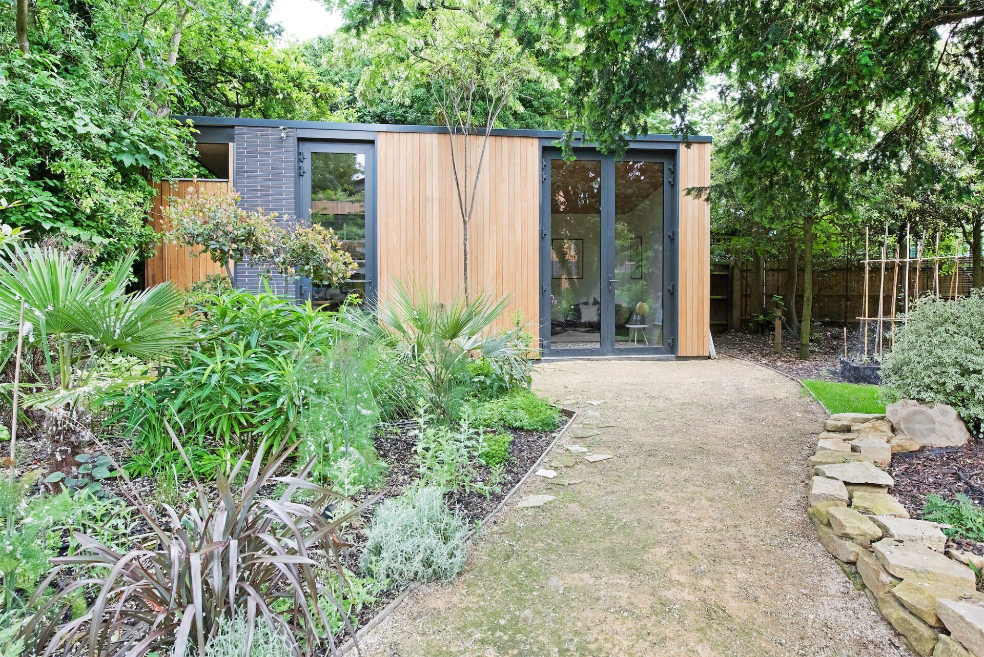 Modern garden office pod with wooden siding, glass door, and surrounding greenery