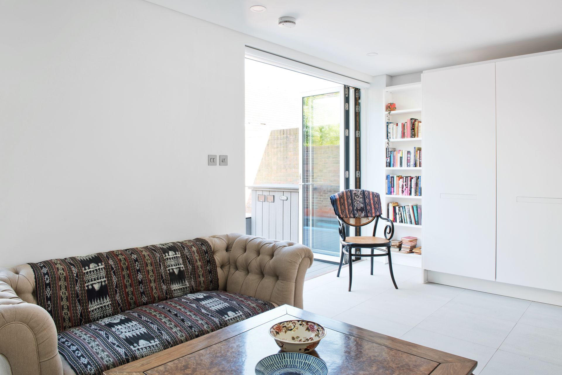 Bright living room with a floral sofa, coffee table, open balcony door, and white wardrobe cabinets