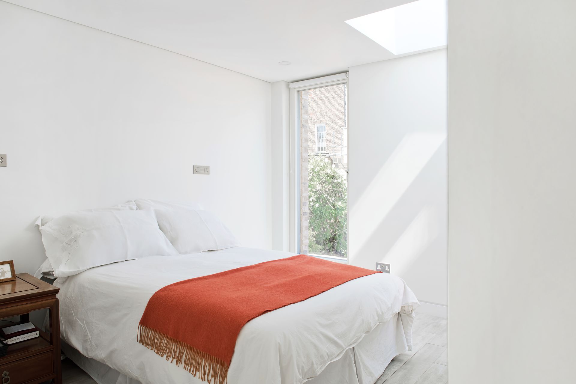 Bright white bedroom with a bed, red throw blanket, and a small window letting in sunlight