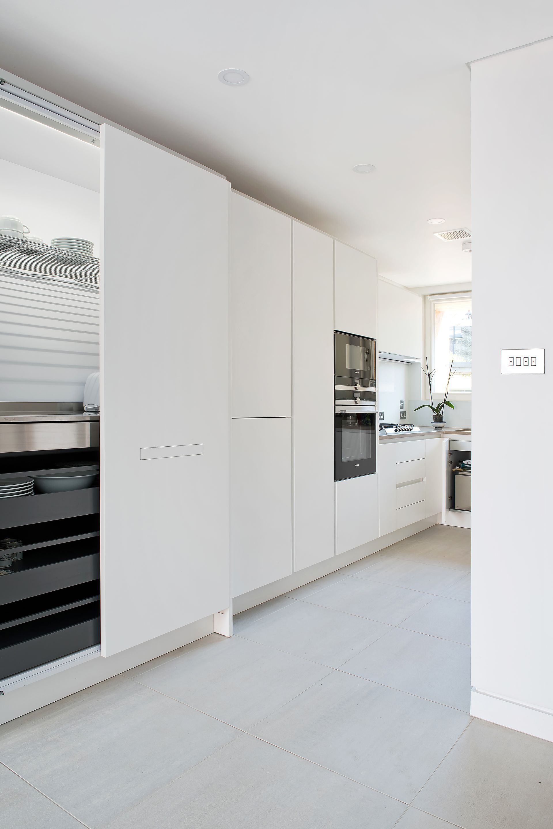 Bright white modern kitchen hallway with built-in appliances and light wood flooring