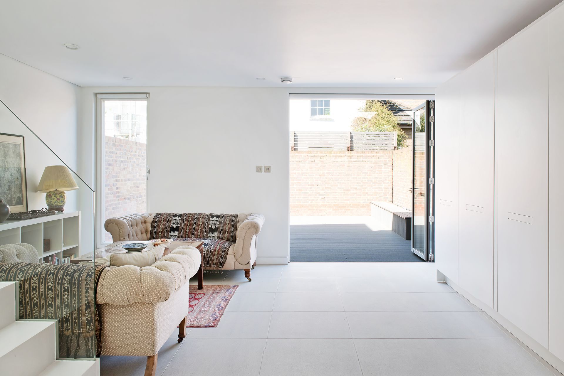 Bright minimalist living room with sofa and lamp, opening to a sunny patio through sliding glass doors