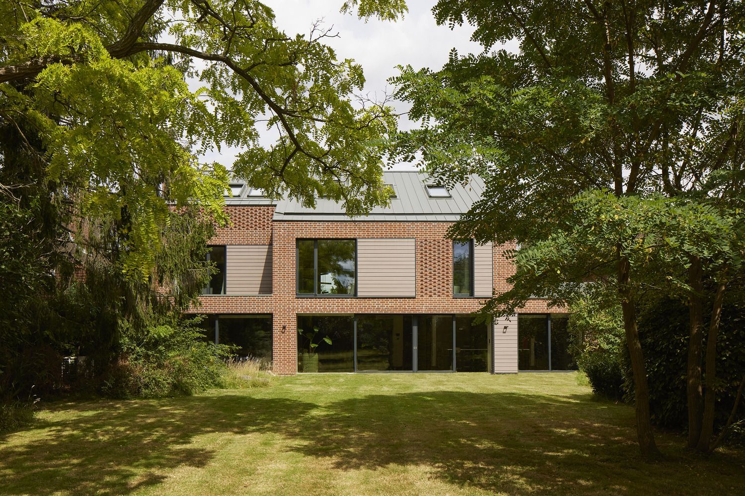 Two-story brick house with large windows, viewed through trees and lawn in the foreground