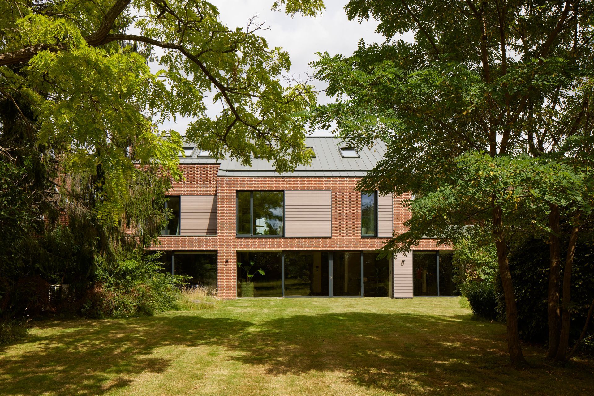 Brick building seen through trees, with a green lawn in front.