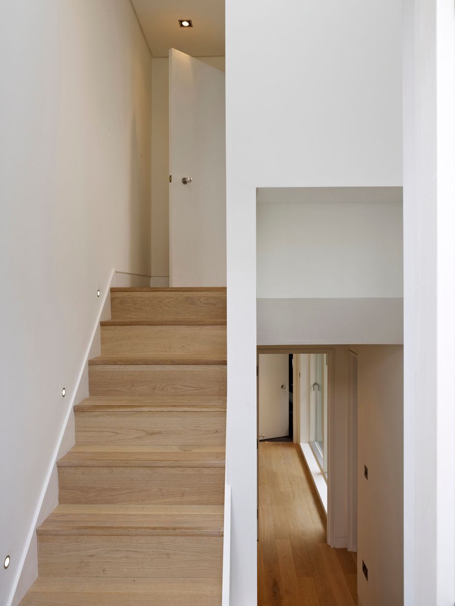 Narrow white staircase beside an interior hallway with light wood flooring and an open door.