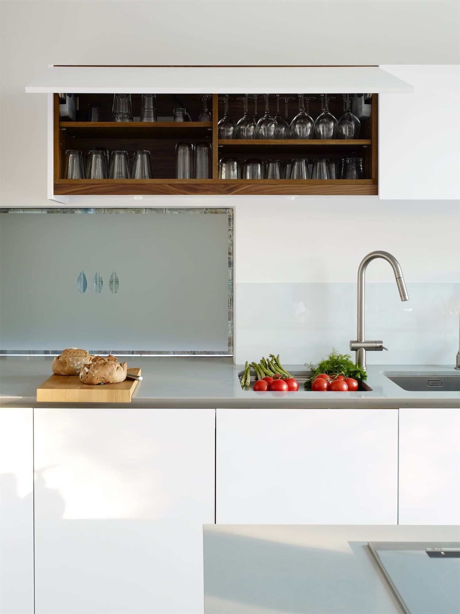 Modern white kitchen with wooden shelves, sink, faucet, cutting board, and fresh produce on the counter