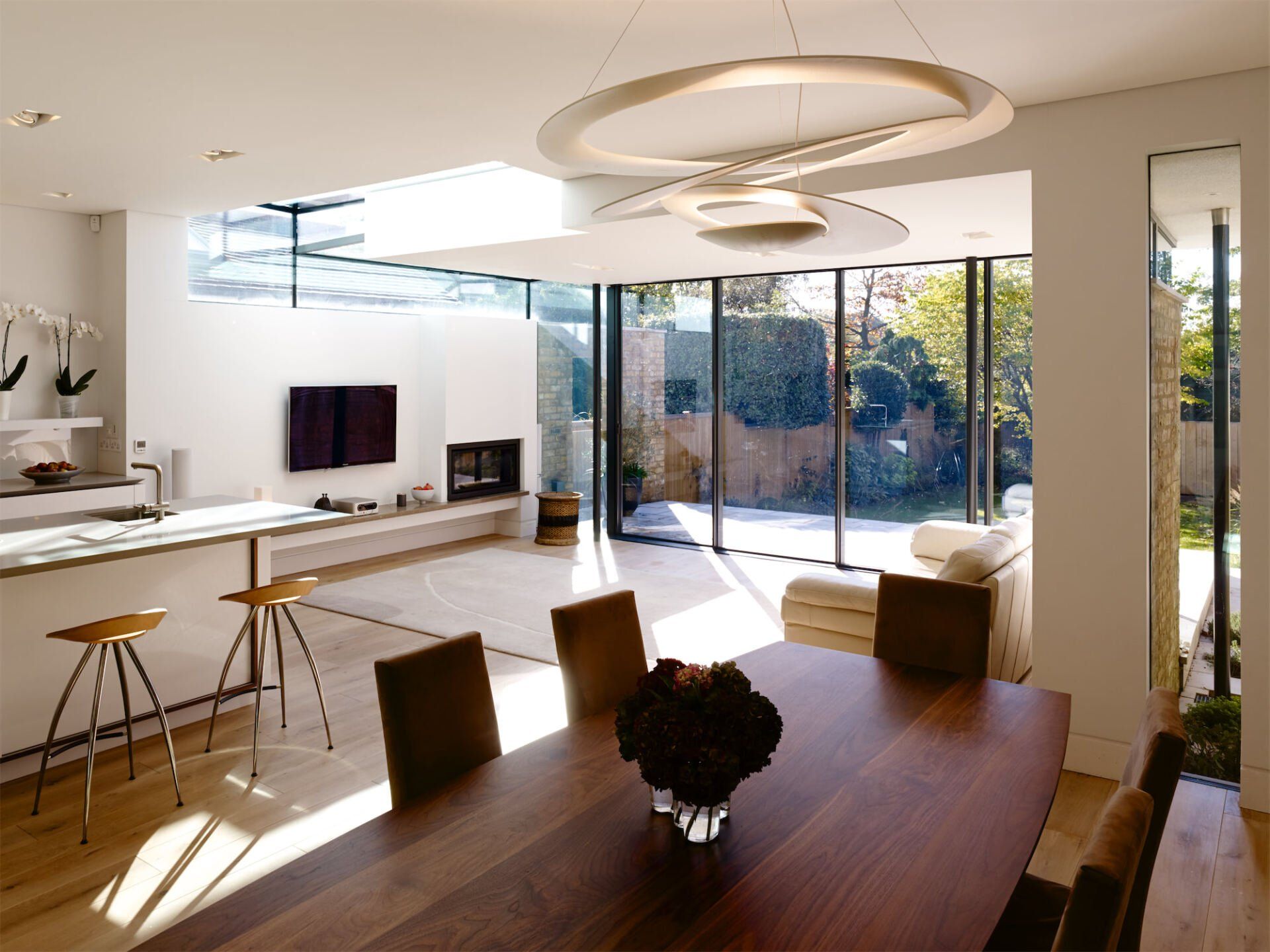Modern open-plan kitchen and dining room with floor-to-ceiling windows and sunlight streaming in