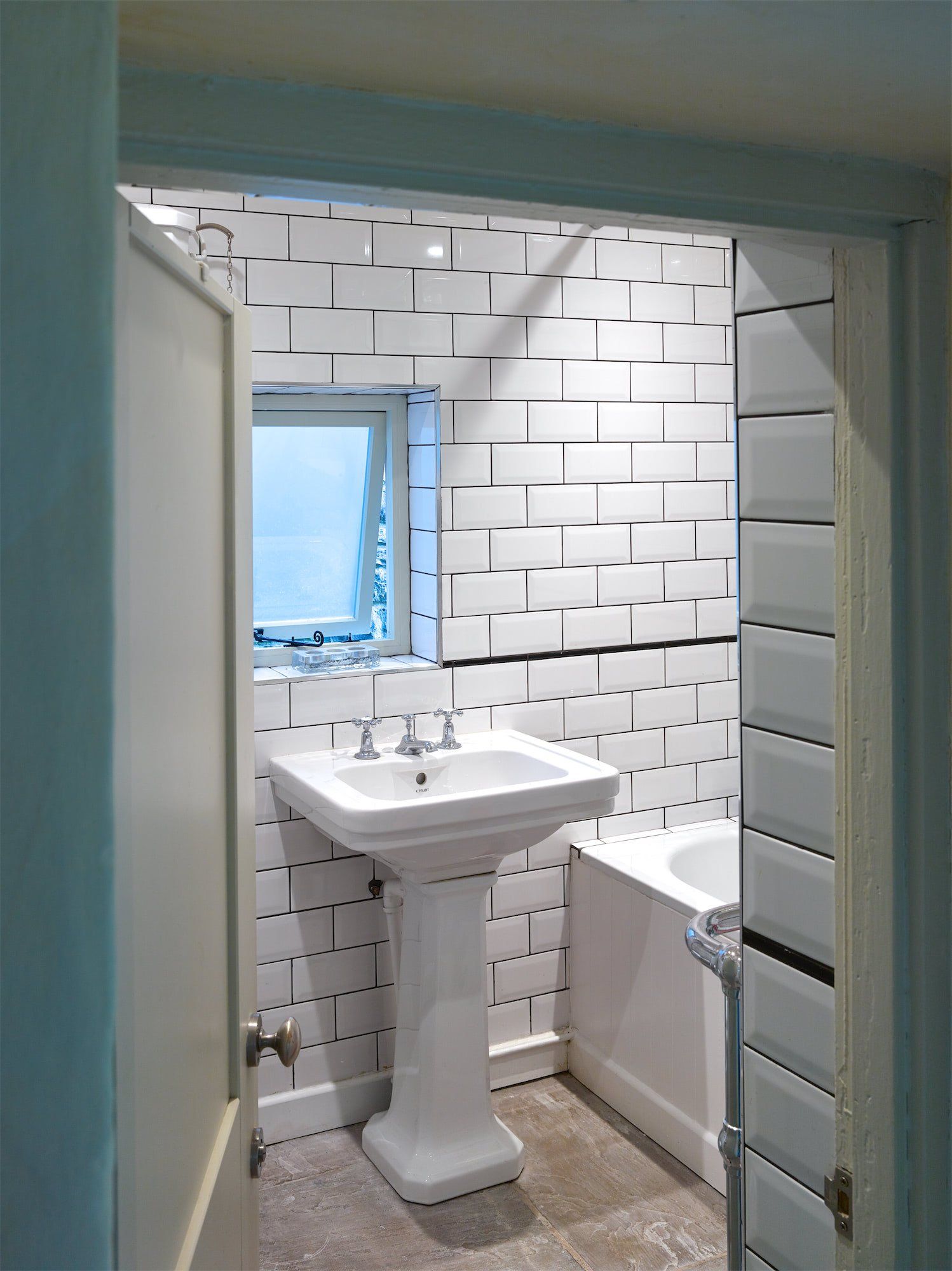 Small white bathroom with pedestal sink, toilet, tiled walls, and a window.