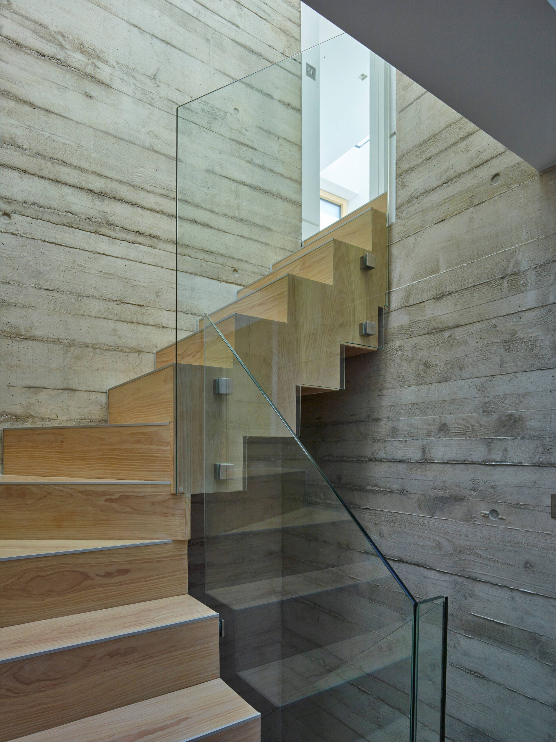 Modern staircase with wood steps, glass railing, and beige stone walls in a minimalist interior