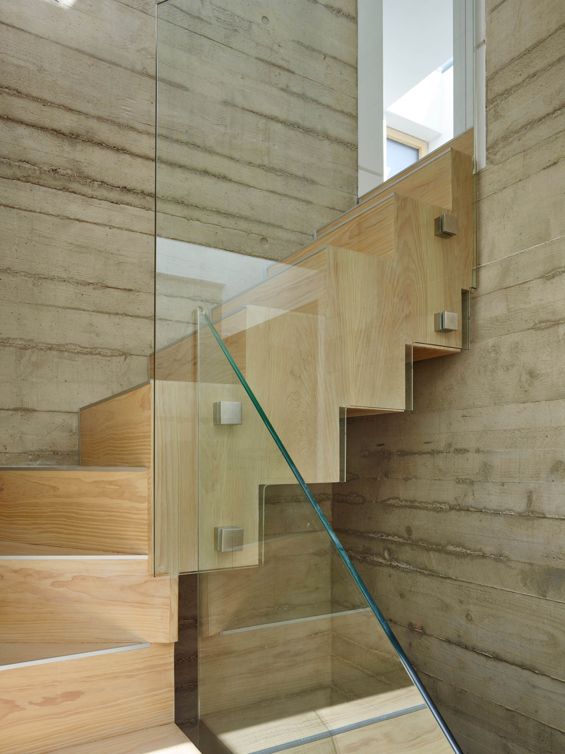 Modern staircase with wood steps, glass railing, and concrete walls in a bright interior.