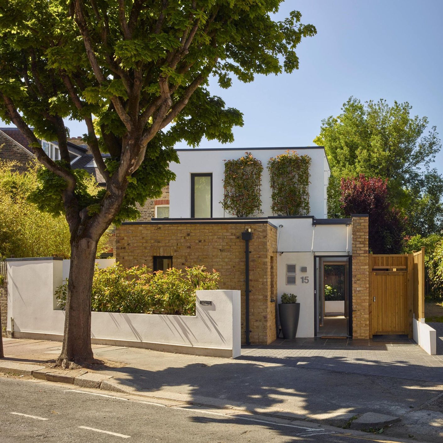 Modern white house with a brick facade, trees, and a sunlit front yard behind a low wall